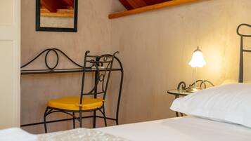Un dormitorio con cama, mesita de noche con lámpara, una silla y espejo en la pared.