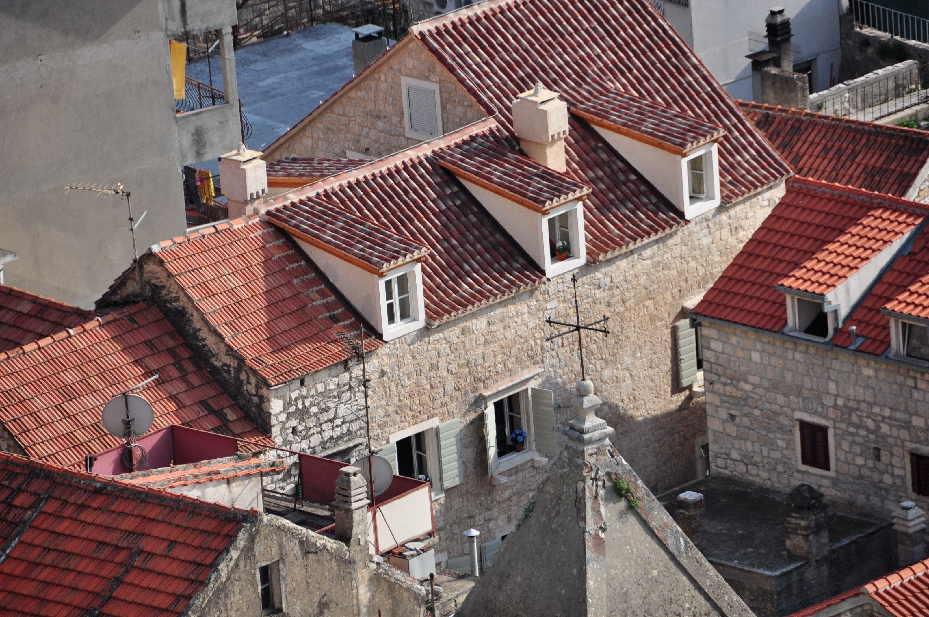 Un edificio de varios pisos con tejados rojos de teja y muros de piedra, que cuenta con numerosas ventanas y balcones.