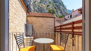 A balcony with a round table and two chairs, a stone wall, and a view of a mountainous landscape. - Vila Mama (Omis)