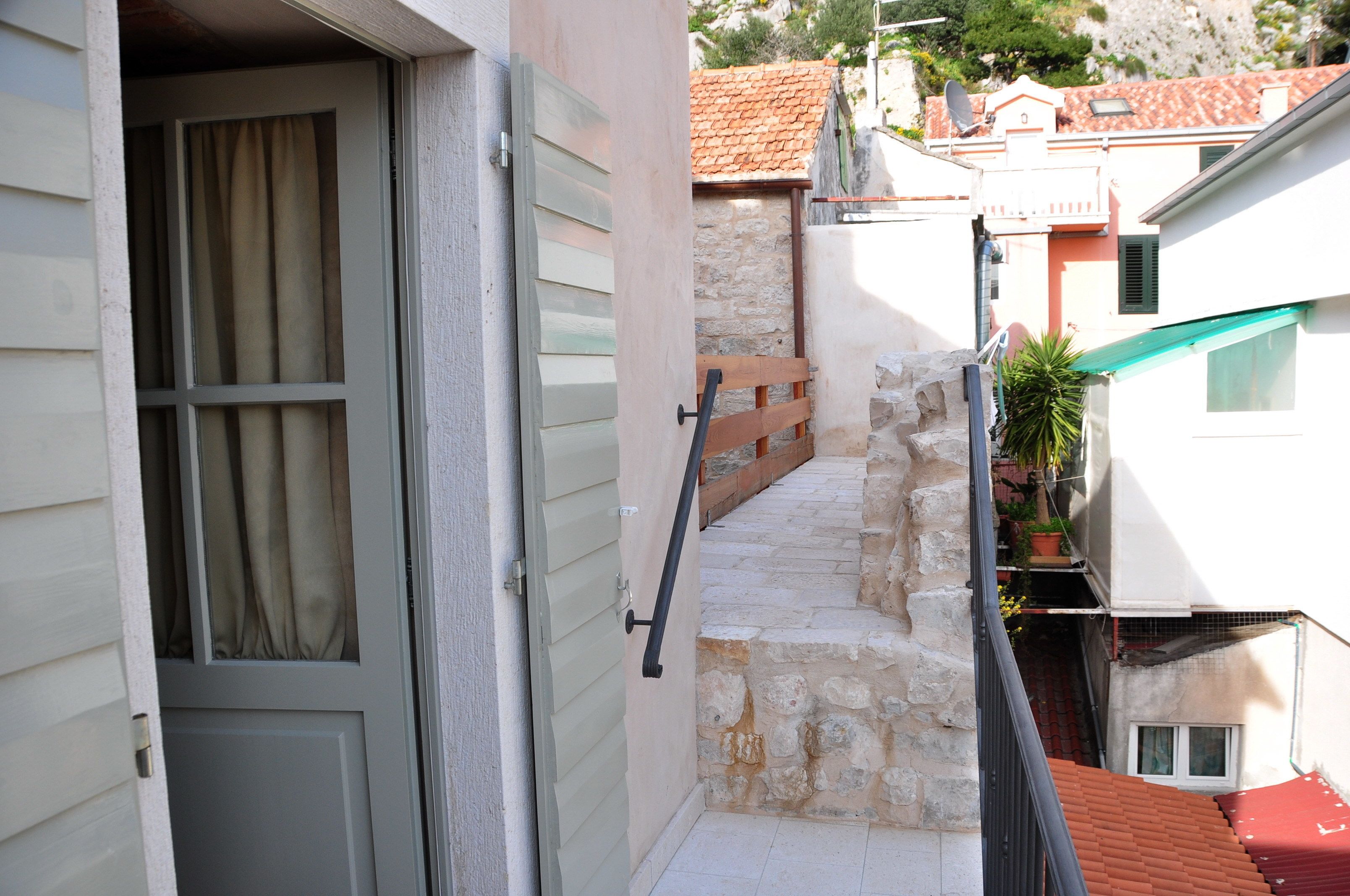 Un escalier étroit en pierre mène à un balcon du deuxième étage, agrémenté d’une rambarde en métal.