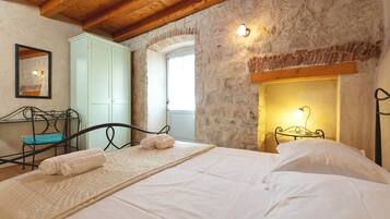 Camera da letto con parete in pietra, soffitto in legno, un letto con lenzuola bianche, un comodino con una lampada e un armadio.