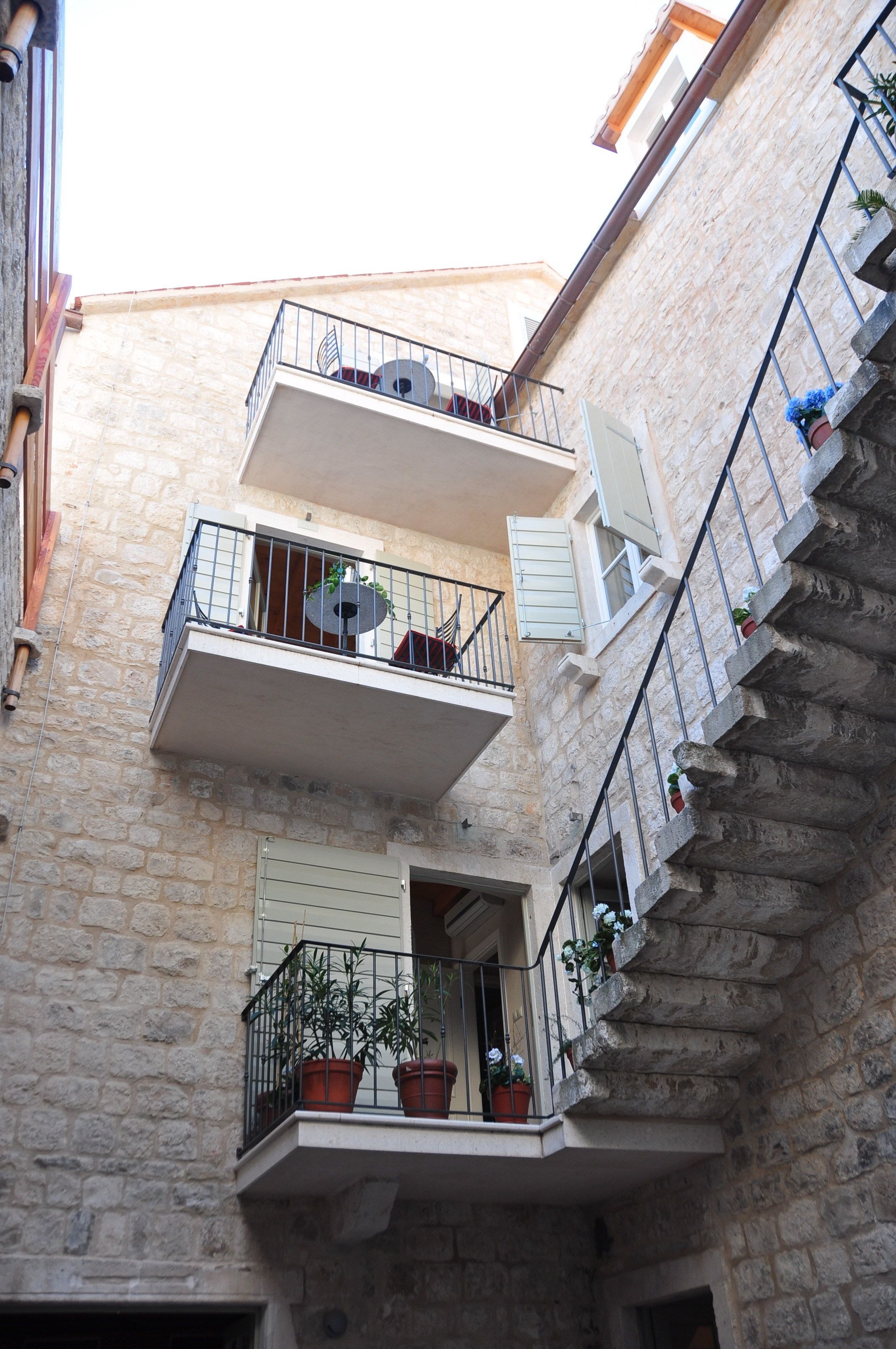Un edificio de varios pisos con paredes de piedra, balcones con barandillas y plantas en macetas.
