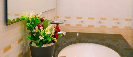Un baño con bañera, lavamanos, espejo y una planta en maceta con flores.