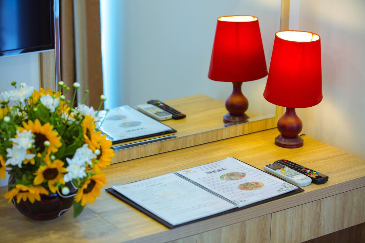 A hotel reception desk with a vase of sunflowers, two red lamps, a menu, and multiple remote controls.