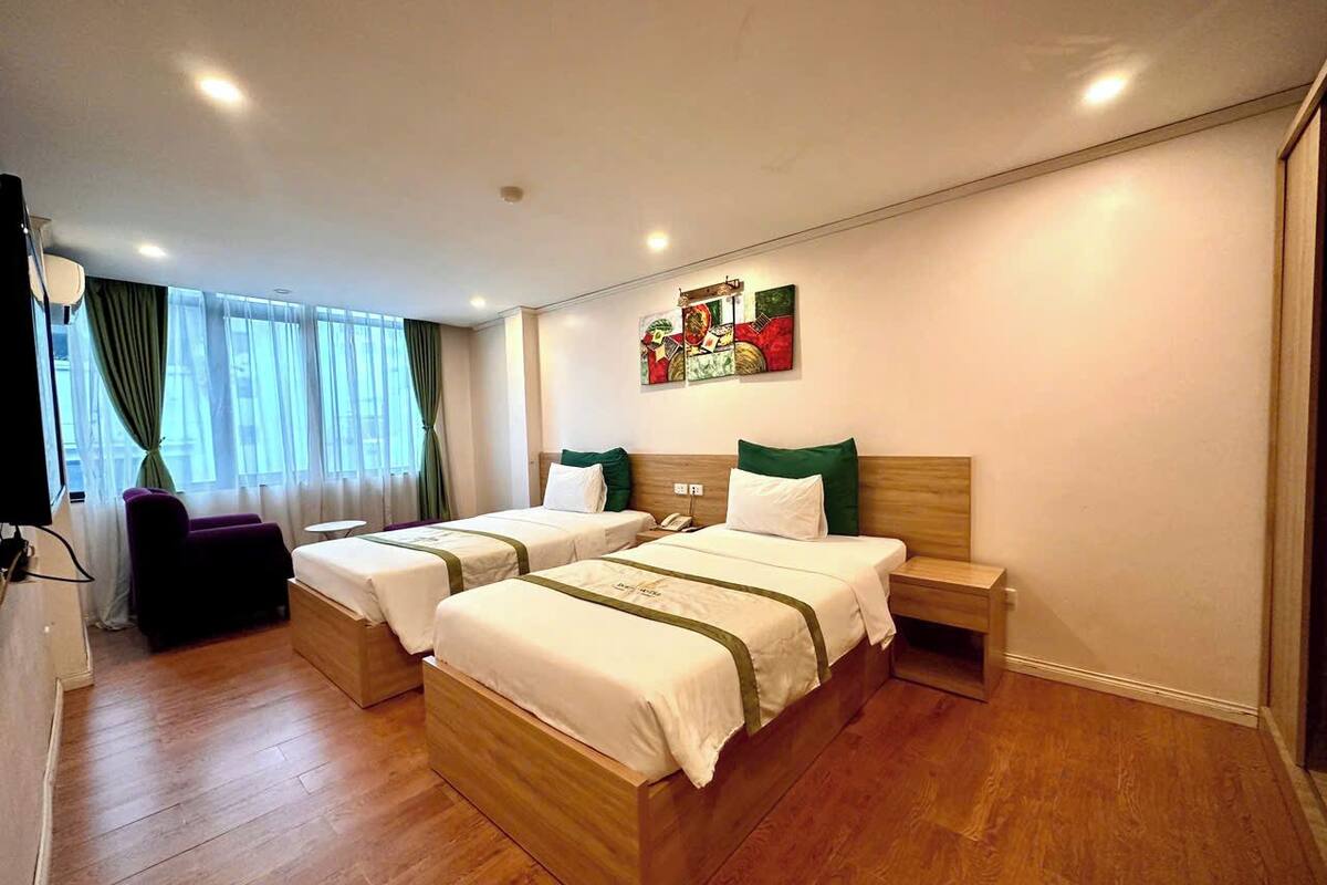 A hotel room with two beds, a small table, a chair, and a painting on the wall.