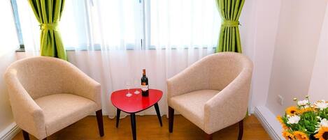 Una habitación con dos sillones color beige, una mesita pequeña con una botella y copas, y un jarrón con flores.