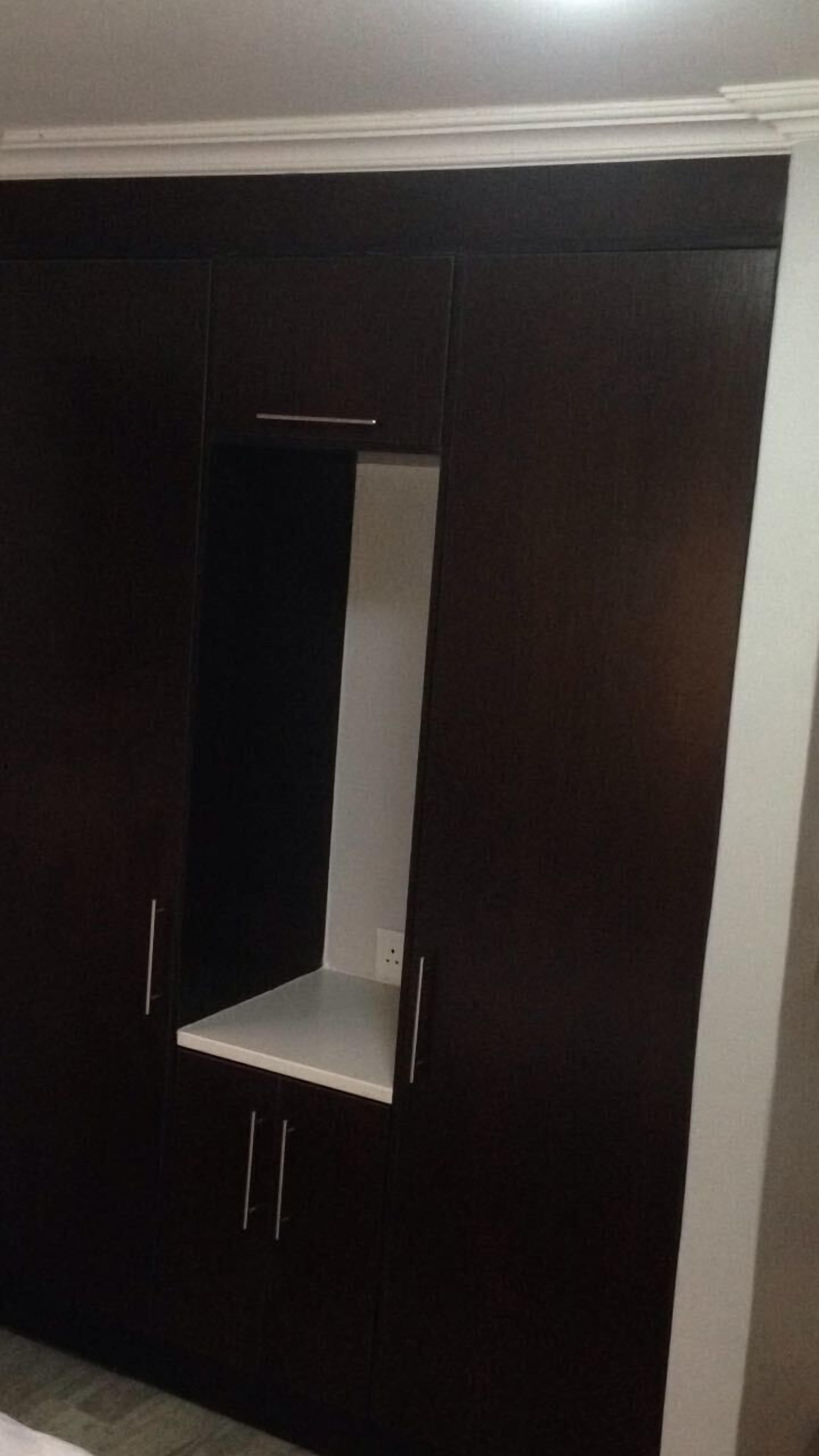 Une armoire en bois foncé avec une étagère blanche et deux poignées.