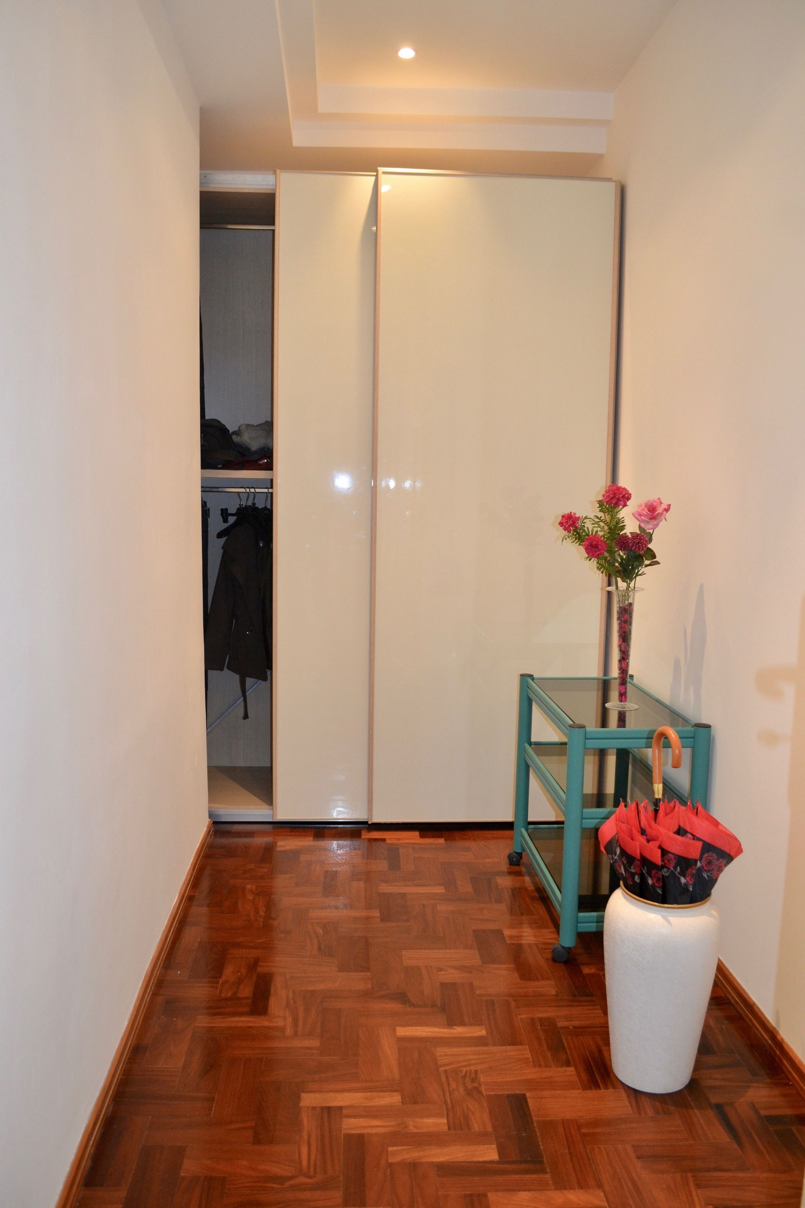 A hallway with a wooden floor, a white closet, and a small table with a vase of flowers.