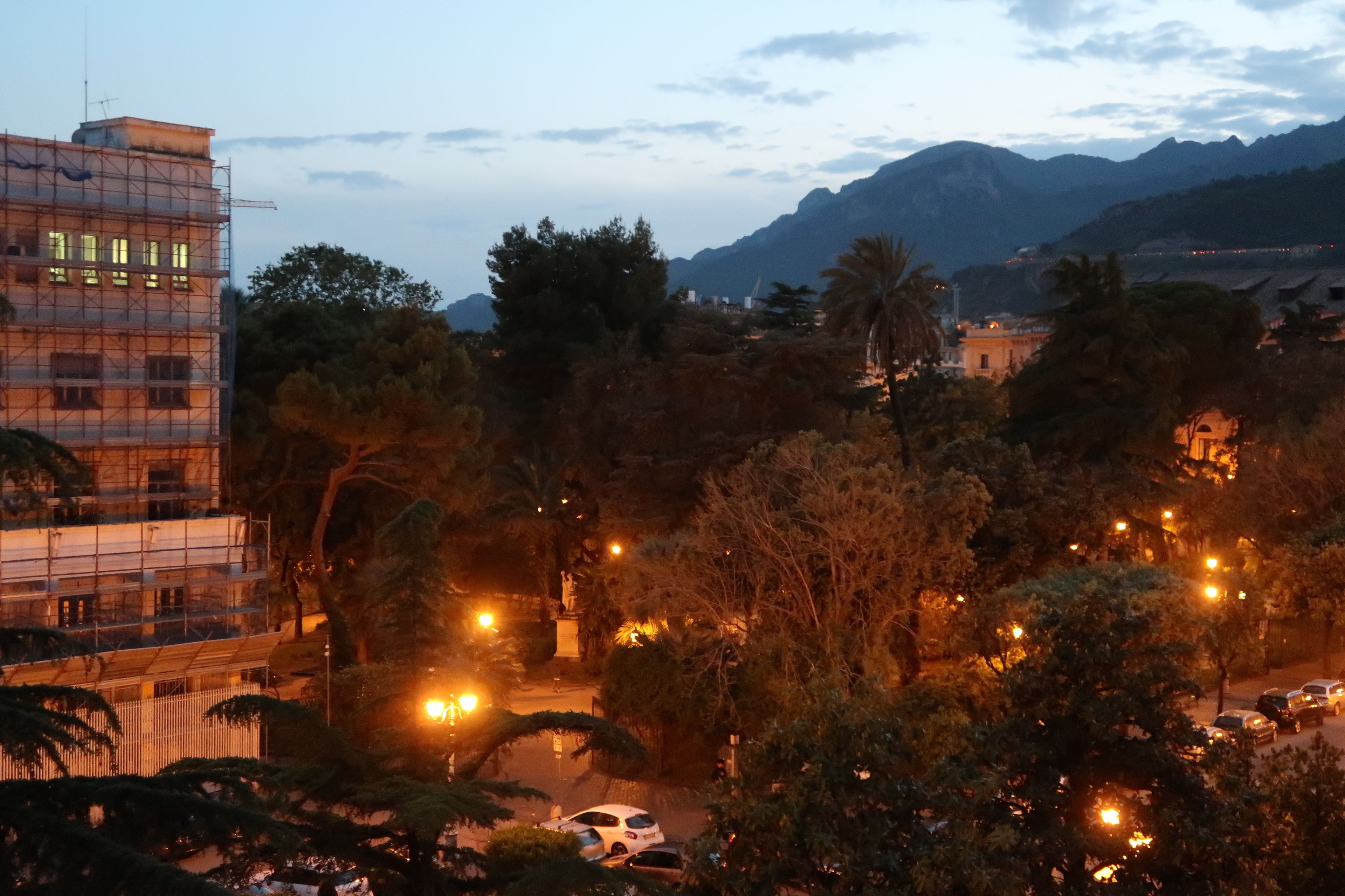 A cityscape at dusk with buildings, trees, and a mountain in the background.