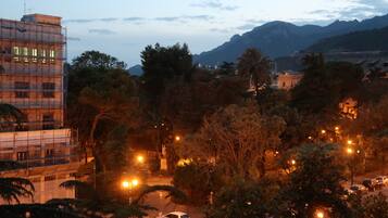 A cityscape at dusk with buildings, trees, and a mountain in the background.