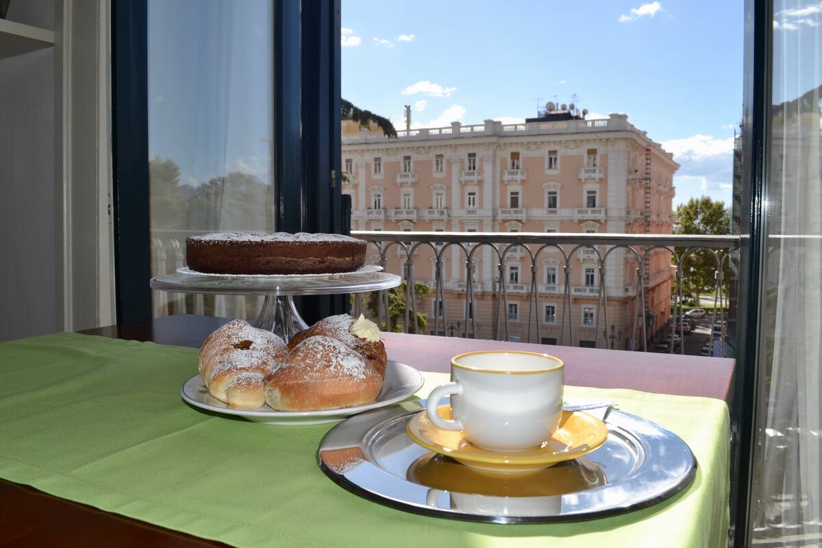 Una mesa con pastel, pastelería y una taza de café en un balcón con vista a un edificio.
