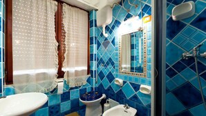 A bathroom with blue tiles, a toilet, a bidet, a sink, and a shower. - Hotel Villa Rosa (Sarroch)