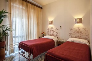 Une chambre d’hôtel avec deux lits, une plante en pot, une fenêtre avec des rideaux et des lampes fixées au mur.