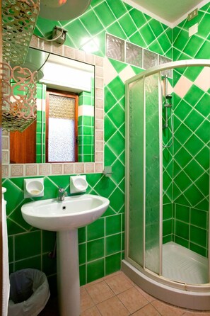 Un baño con azulejos verdes, un lavabo blanco y una ducha con mampara de vidrio.