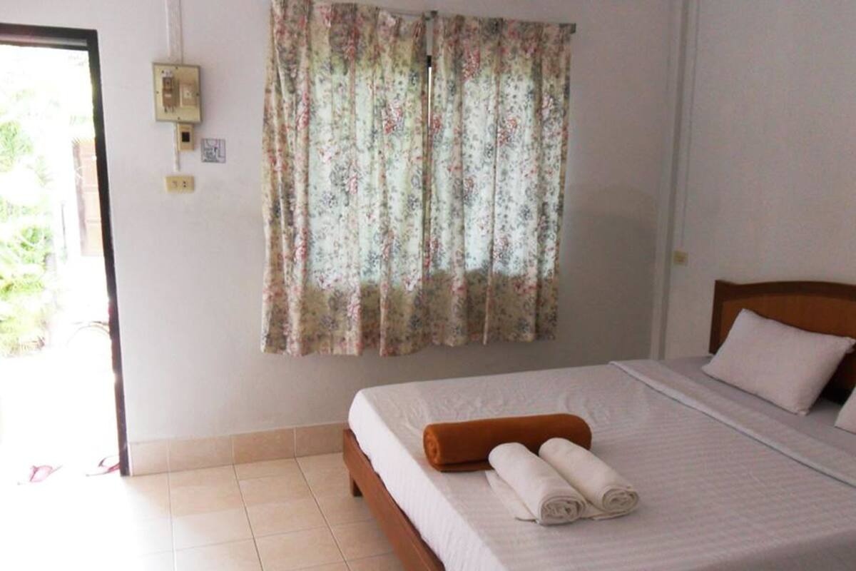 Quarto com uma cama, cabeceira de madeira, toalha enrolada e cortina florida.
