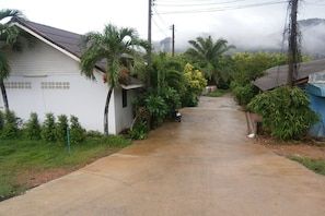 A residential street with houses, palm trees, and a cloudy sky. - Aonang SR Bungalow (Krabi)