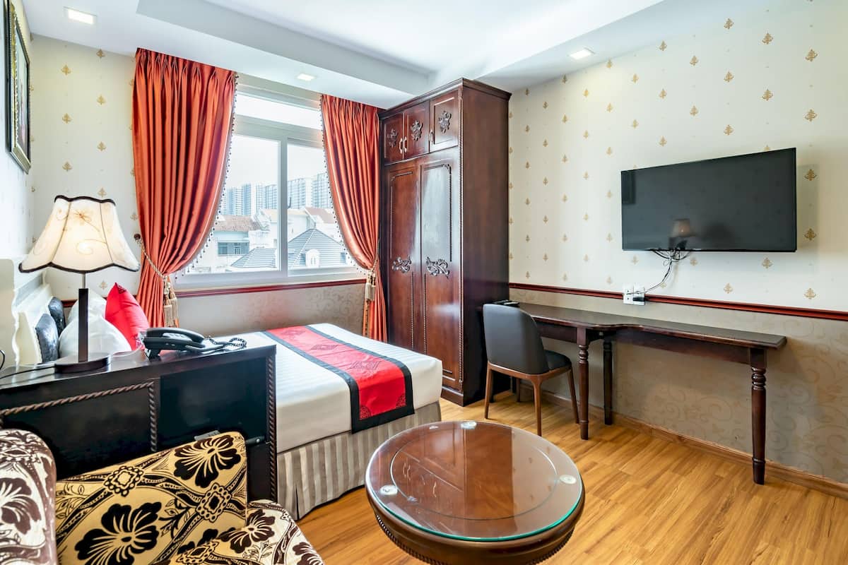 Een hotelkamer met een bed, bureau, televisie en uitzicht op de stad.