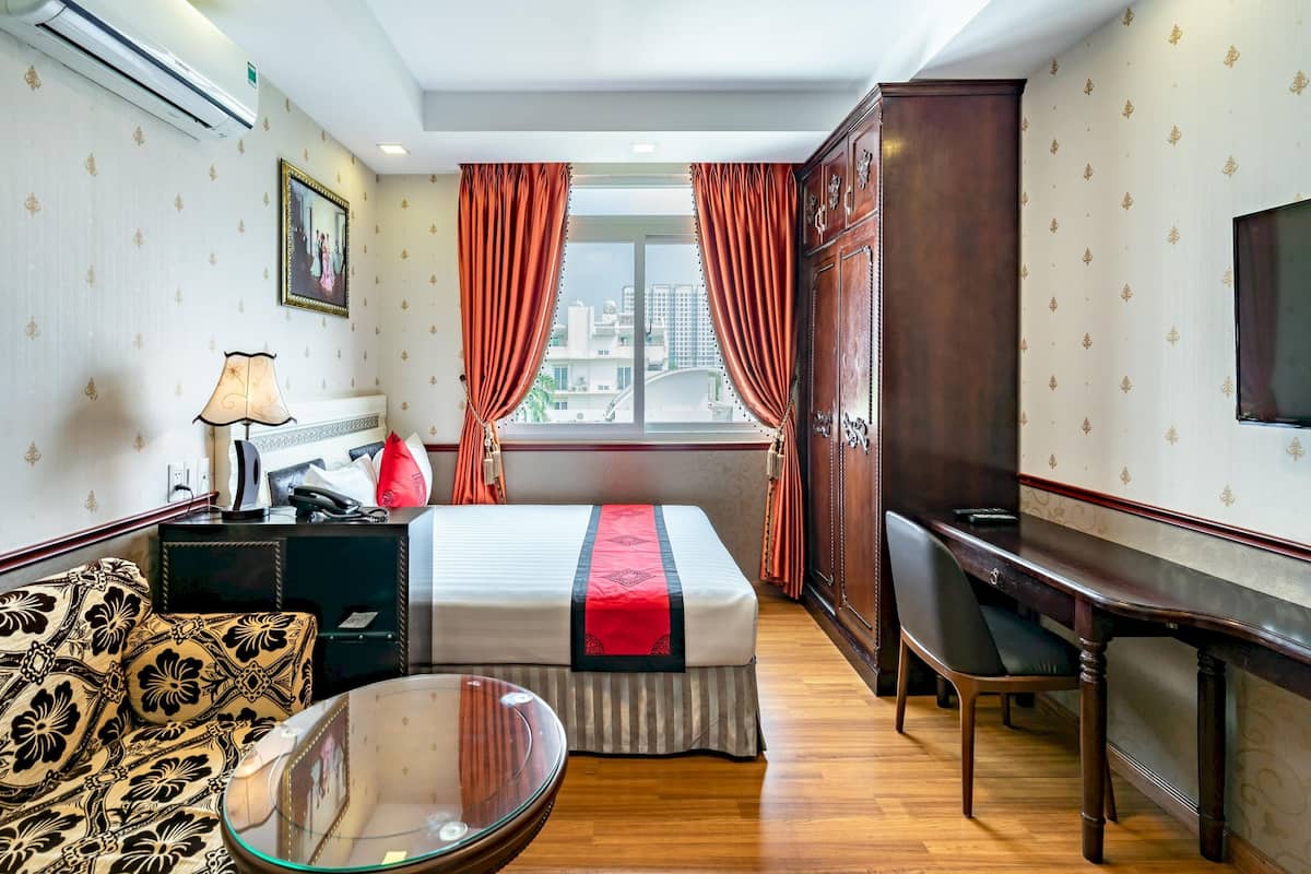 Een hotelkamer met een bed, een bureau, een bank, een televisie en een raam met gordijnen.
