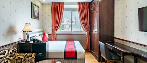 A hotel room with a bed, a desk, a sofa, a TV, and a window with curtains.