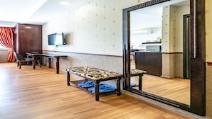 A hotel room with a wooden floor, a large mirror, a TV mounted on the wall, and a dining area with a bench and chairs. - Collection O Emerald Luxury Apartment - Near SECC (Ho Chi Minh City)