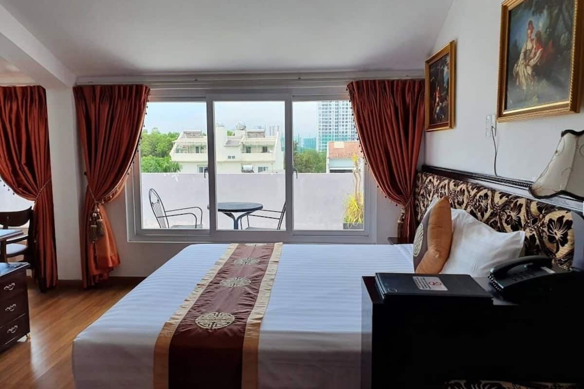 Een hotelkamer met een groot bed, een bureau, een stoel en uitzicht op de stad door een groot raam.