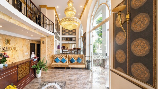 A hotel lobby with a reception desk, a chandelier, a sofa, and a large decorative wall. - Collection O Emerald Luxury Apartment - Near SECC (Ho Chi Minh City)