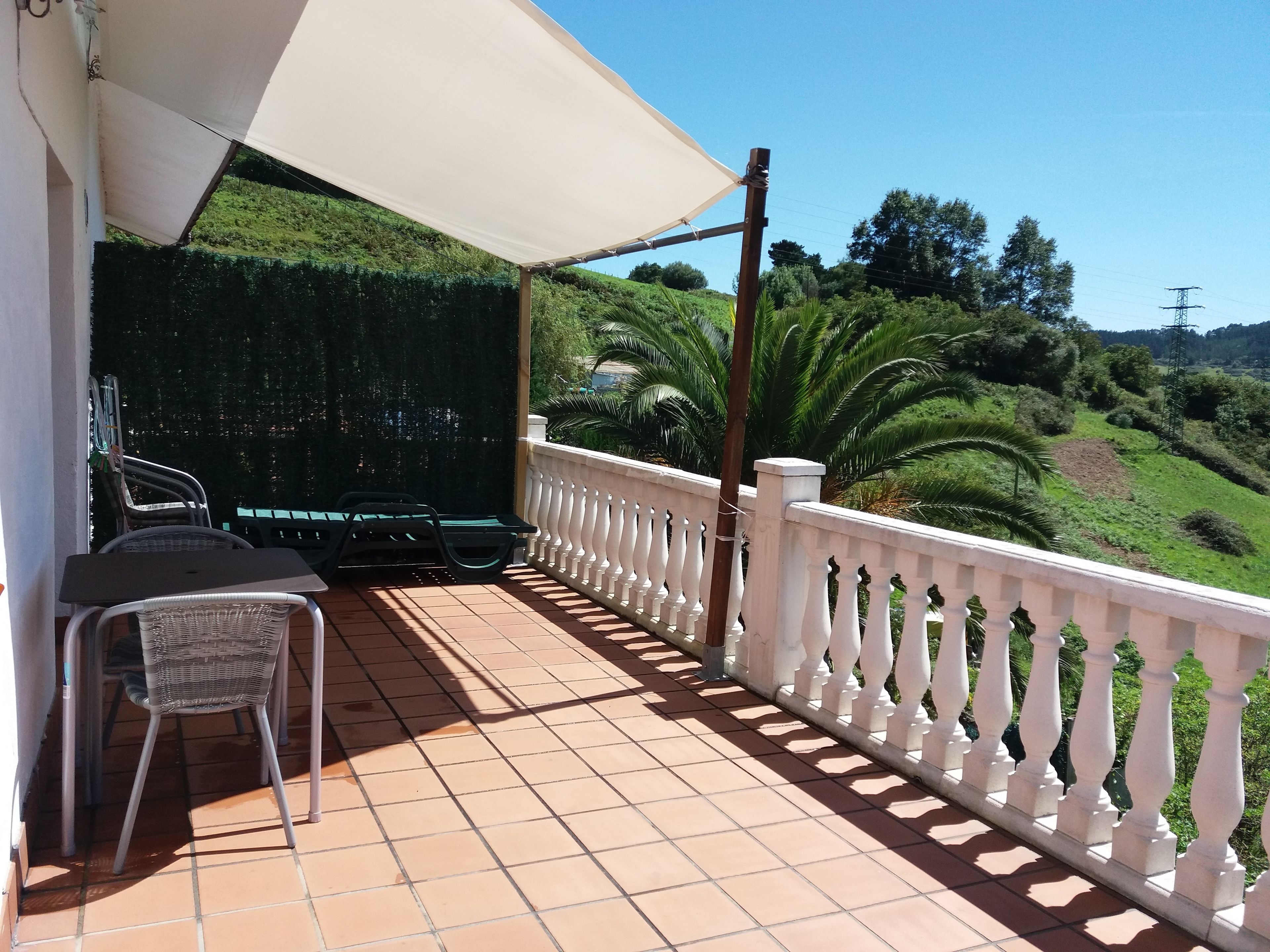 Un balcon doté d’une balustrade blanche, d’une table, de chaises et d’un grand parasol.