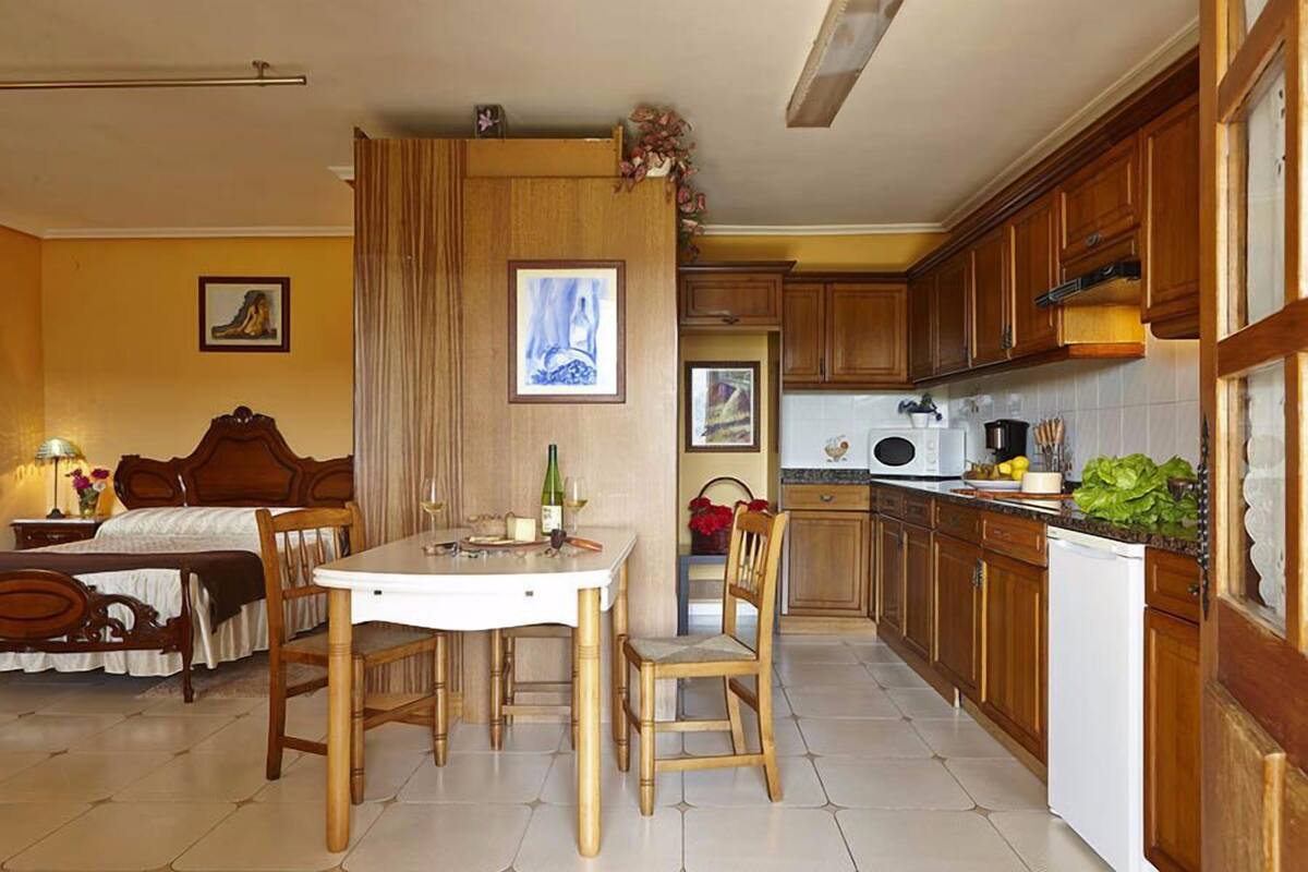 Une chambre d’hôtel comprenant un lit, une table à manger avec des chaises, un coin cuisine avec des placards en bois et un four à micro-ondes.