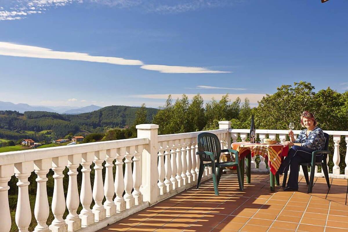 Une terrasse dotée d’une balustrade blanche, une table recouverte d’une nappe et une personne assise à cette table.