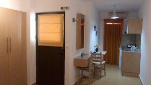 A compact living space with a kitchenette, a dining area, and a door with a window blind.