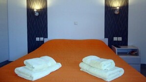 A hotel room with an orange bedspread, two white towels folded on the bed, and wall-mounted light fixtures.
