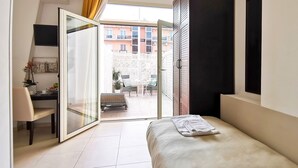 Un dormitorio con cama, escritorio y silla. Posee una puerta corrediza de vidrio que da a un espacio al aire libre con mesa y sillas.
