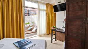 Habitación de hotel con cama, escritorio, televisor y balcón con cortinas amarillas.
