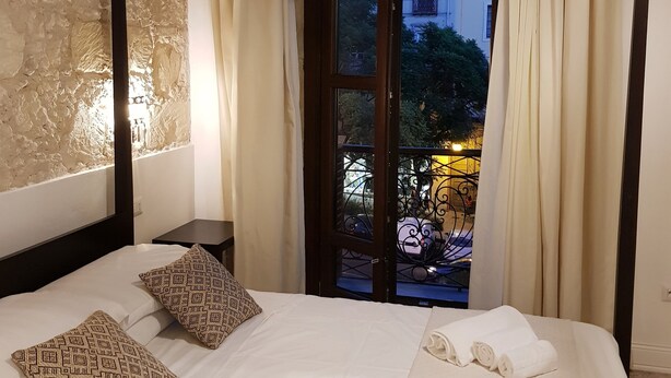 A hotel room with a large bed, two patterned pillows, a nightstand, and a view of a courtyard with a building and trees. - La Residenza sul Largo (Cagliari)