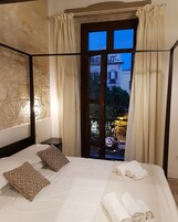Habitación de hotel con una cama grande, dos almohadas estampadas, una mesita de noche y vistas a un patio con un edificio y árboles.