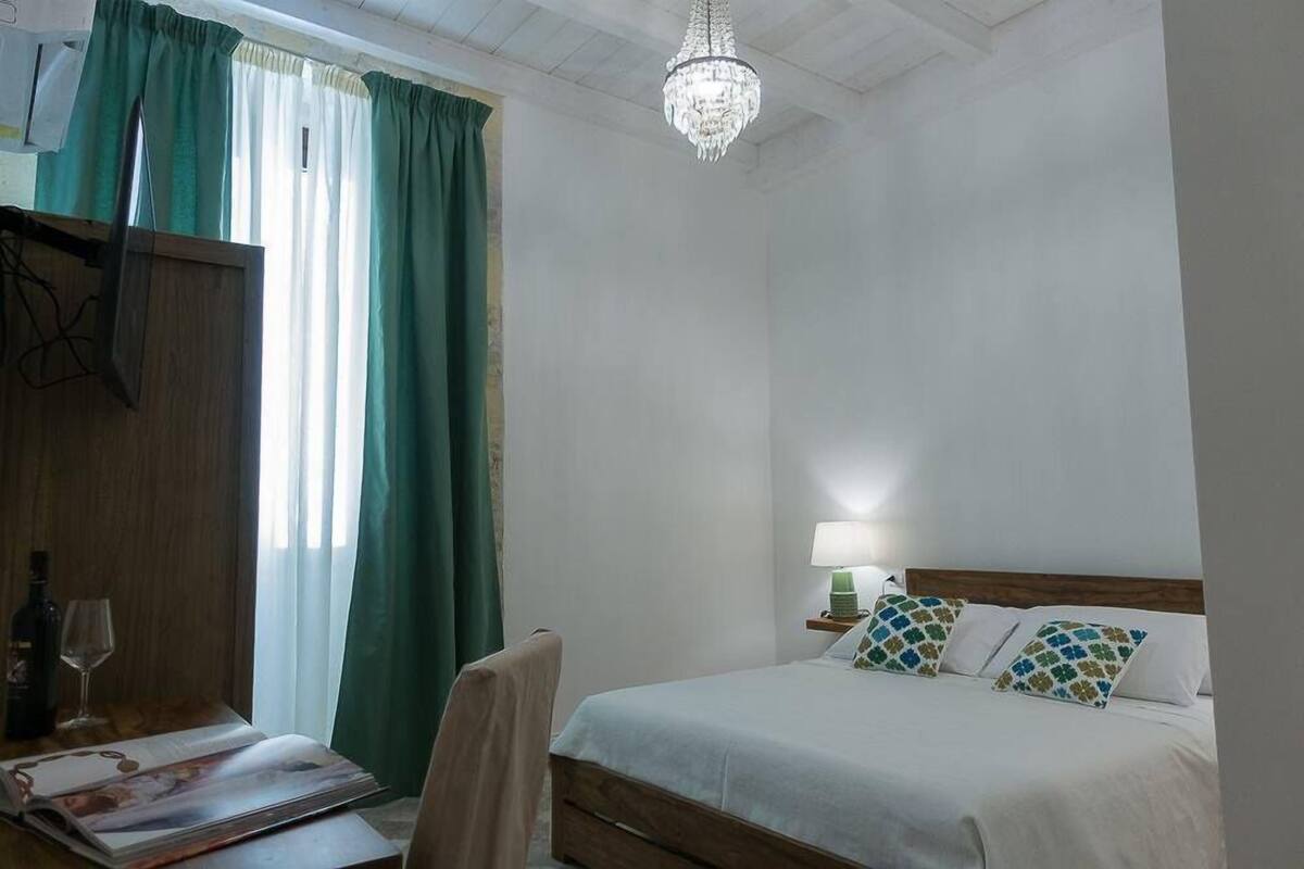 A hotel room with a bed, a desk with a chair, a lamp, and a chandelier.
