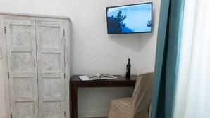 A room with a white wardrobe, a wooden desk with a book and a bottle, a TV on the wall, and a beige chair. - La Residenza sul Largo (Cagliari)