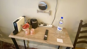 Une petite table en bois, avec un téléviseur à écran plat fixé au-dessus, un miroir, une multiprise, une télécommande, une bouteille d’eau et quelques tasses.