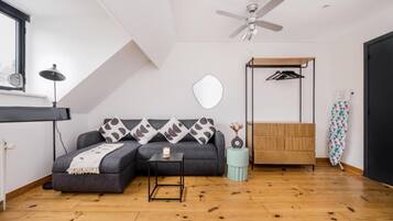 A modern room with a sofa, a small table, a ceiling fan, a hanging clothes rack, and a wooden floor.