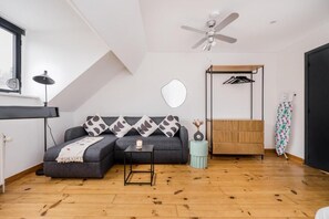 A modern room with a sofa, a small table, a ceiling fan, a hanging clothes rack, and a wooden floor. - Simone's Kitchen B&B (Antwerp)