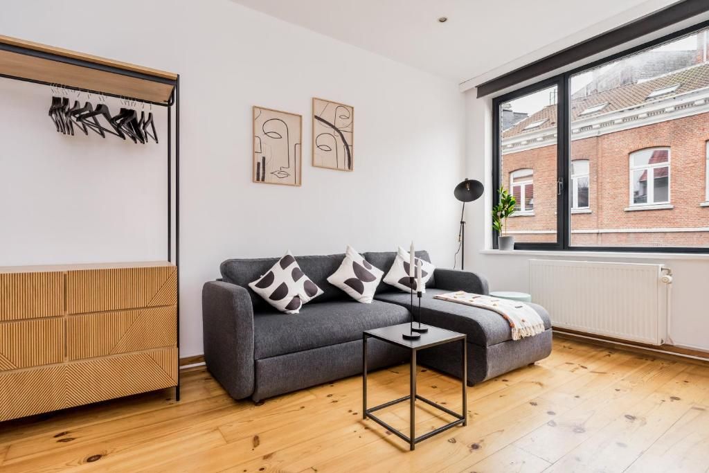 Un salon moderne avec un canapé gris, une petite table et une fenêtre donnant sur un bâtiment en briques.