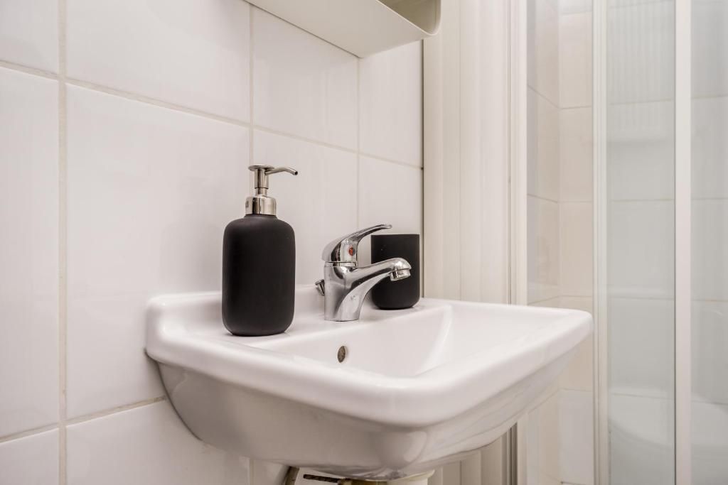 Un lavabo blanc pour la salle de bain, doté d’un robinet chromé et d’un distributeur de savon noir.
