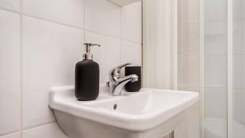 Un lavabo blanc pour la salle de bain, doté d’un robinet chromé et d’un distributeur de savon noir.