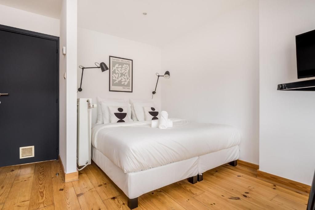 Une chambre à coucher avec un lit, deux lampes de chevet, un tableau encadré et un téléviseur fixé au mur.