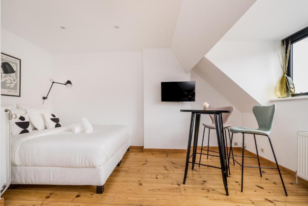 A bedroom with a bed, a desk, two chairs, a television, and a window with curtains.