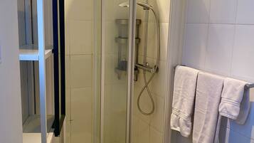 A glass-enclosed shower with a handheld showerhead, a wall-mounted towel rack with towels, and a white sink with a chrome faucet.