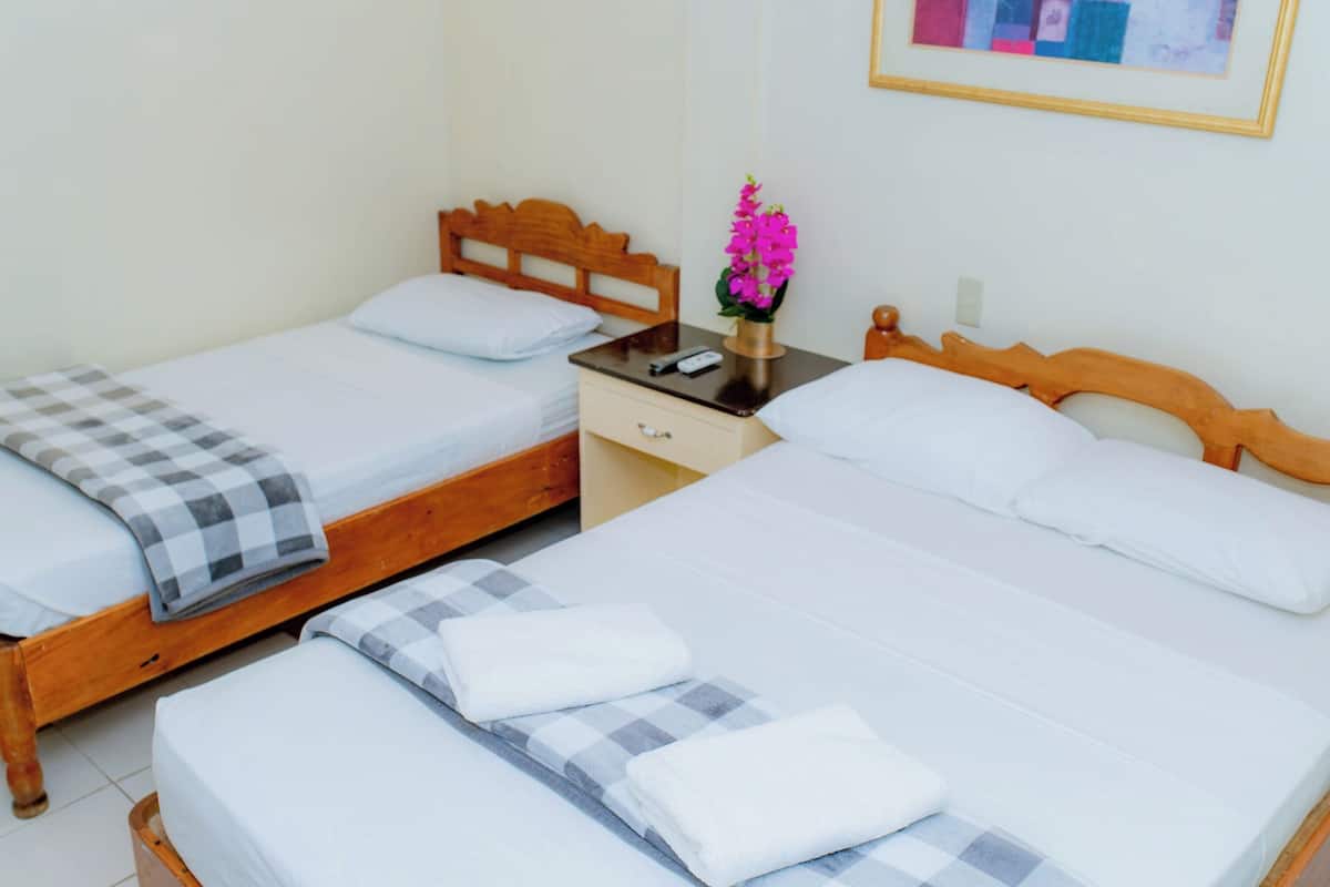 Habitación de hotel con dos camas individuales, un cabecero de madera, una mesita de noche con un jarrón de flores y un cajón pequeño.