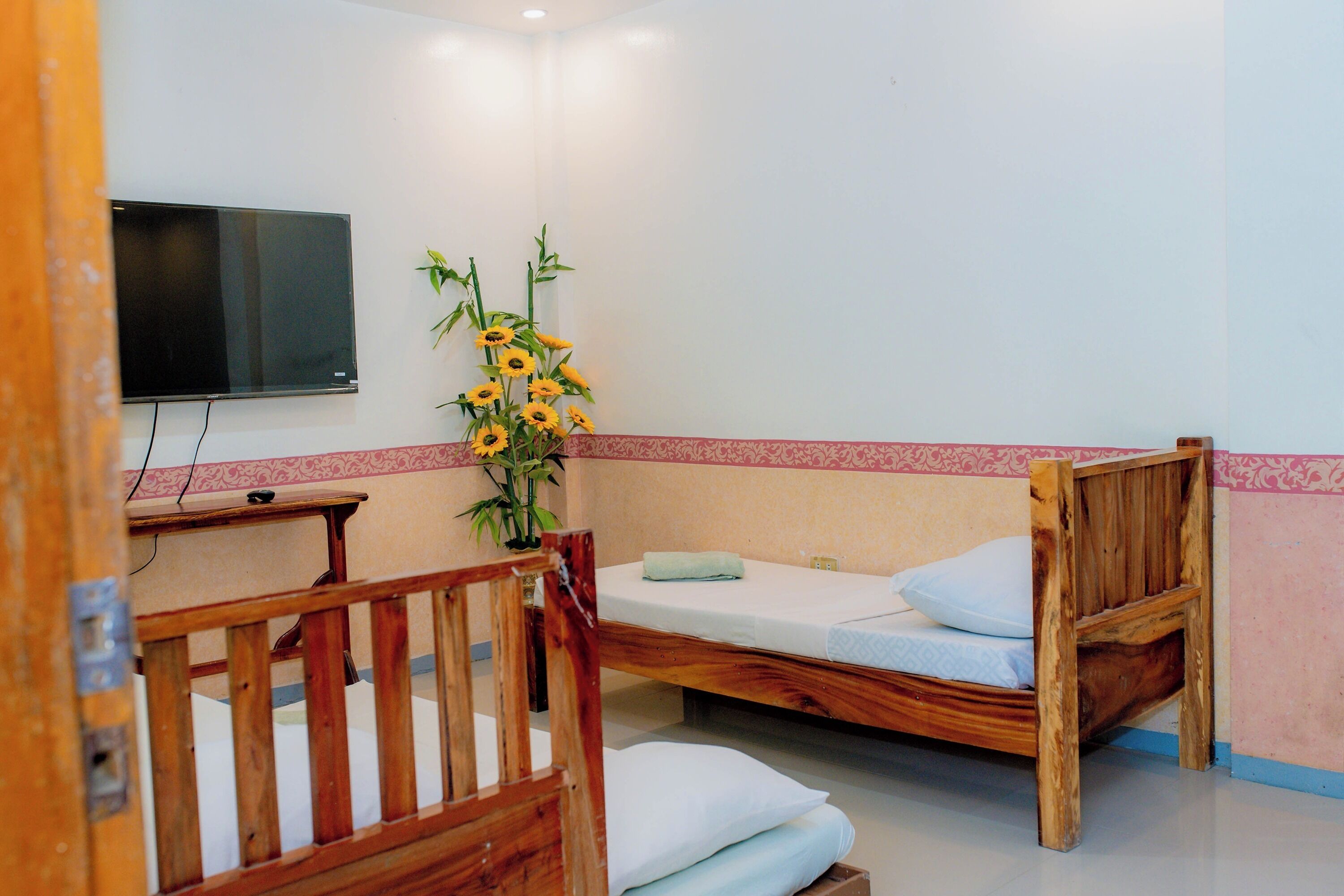A bedroom with two wooden beds, a TV mounted on the wall, and a vase with sunflowers.