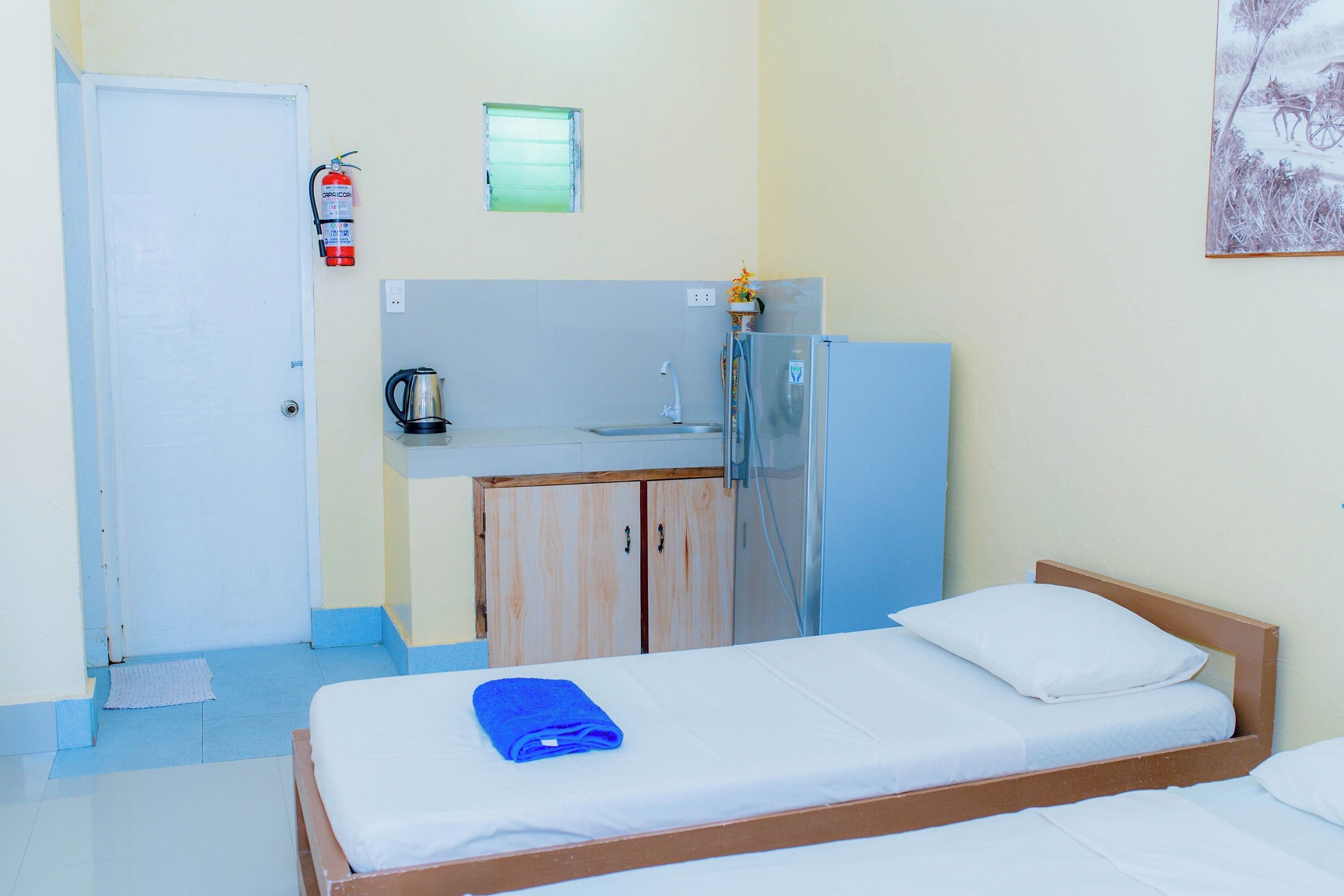 A room with a bed, a small kitchenette, a door, and a window.