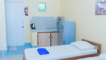 A room with a bed, a small kitchenette, a door, and a window.